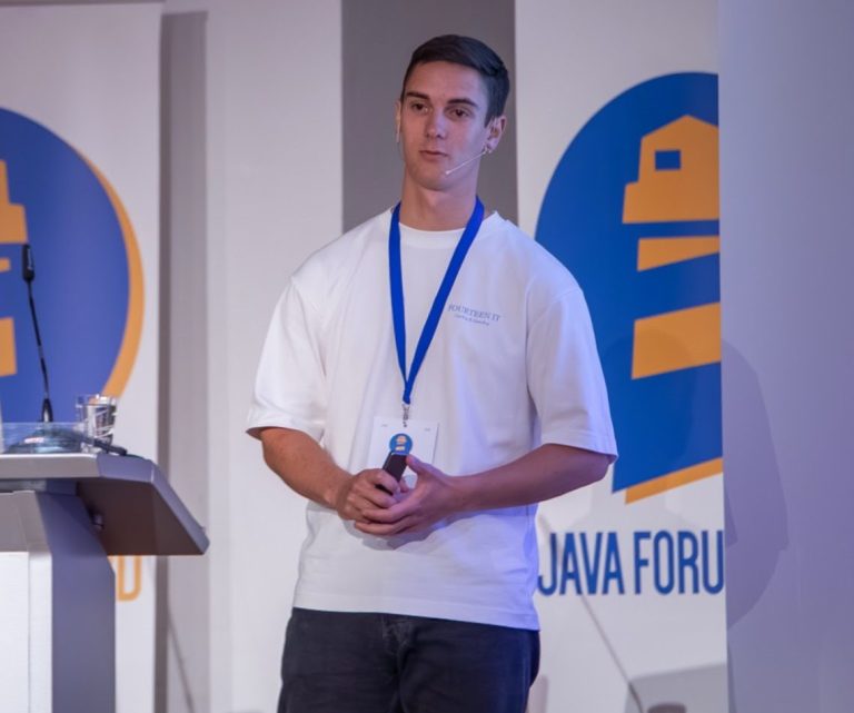 Ein Mann mit Speaker-Badge steht an einem Rednerpult auf einer Konferenzbühne.